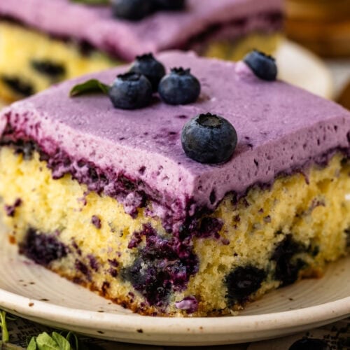 Slice of Blueberry Chantilly Sheet Cake topped with fluffy blueberry frosting and fresh blueberries.