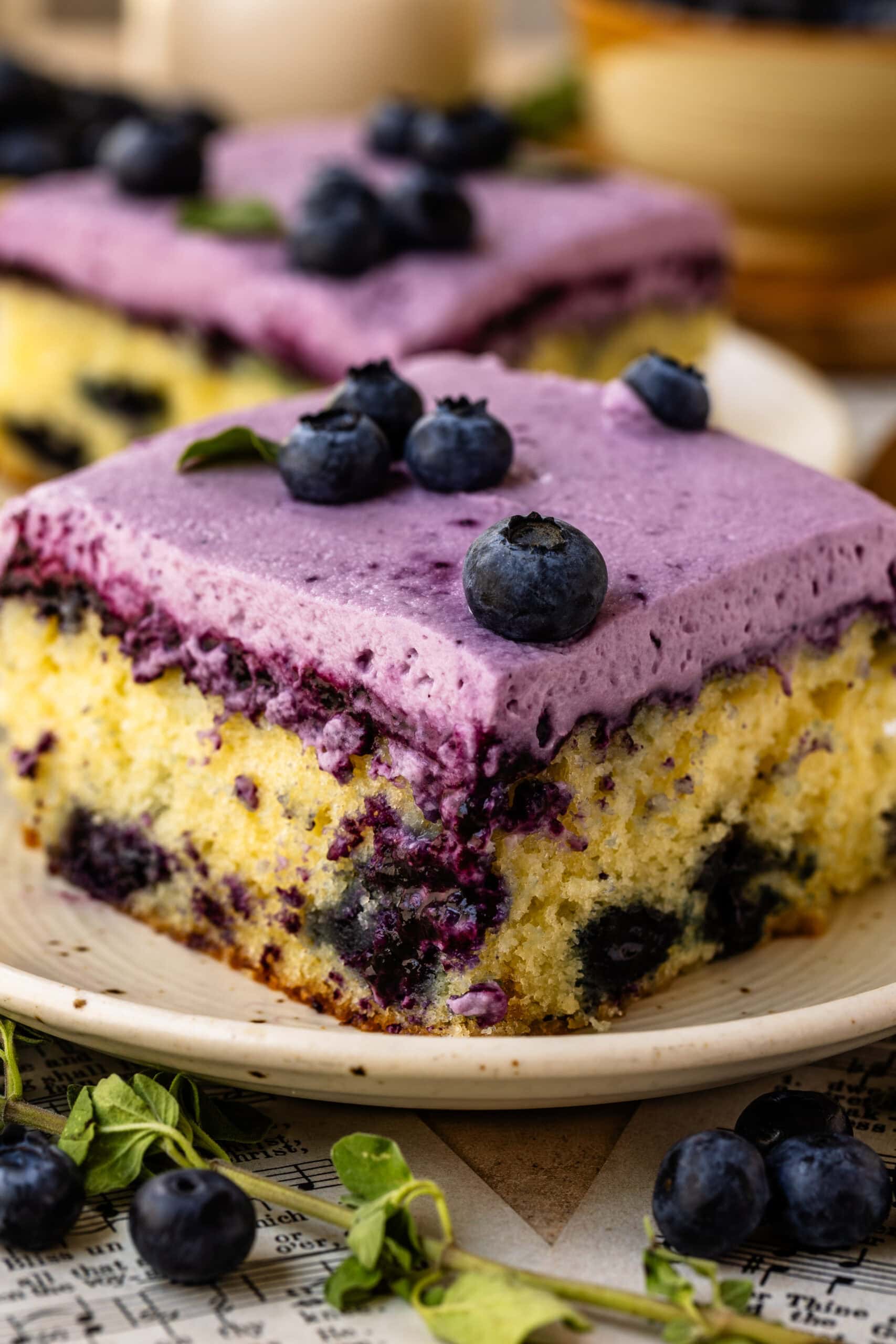 Slice of Blueberry Chantilly Sheet Cake topped with fluffy blueberry frosting and fresh blueberries.