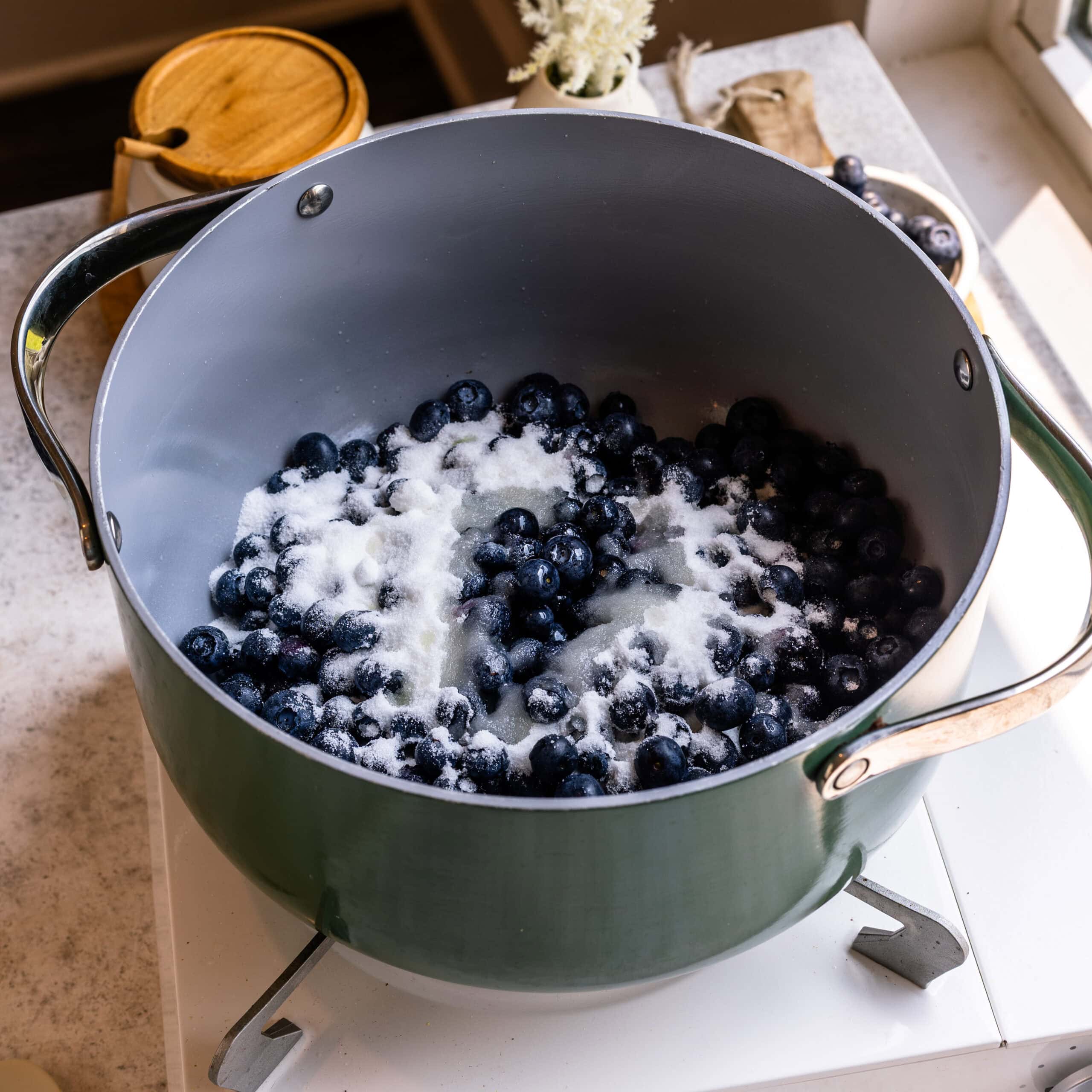 Blueberries and sugar in a large sauce pot on the stove to make blueberry sauce.