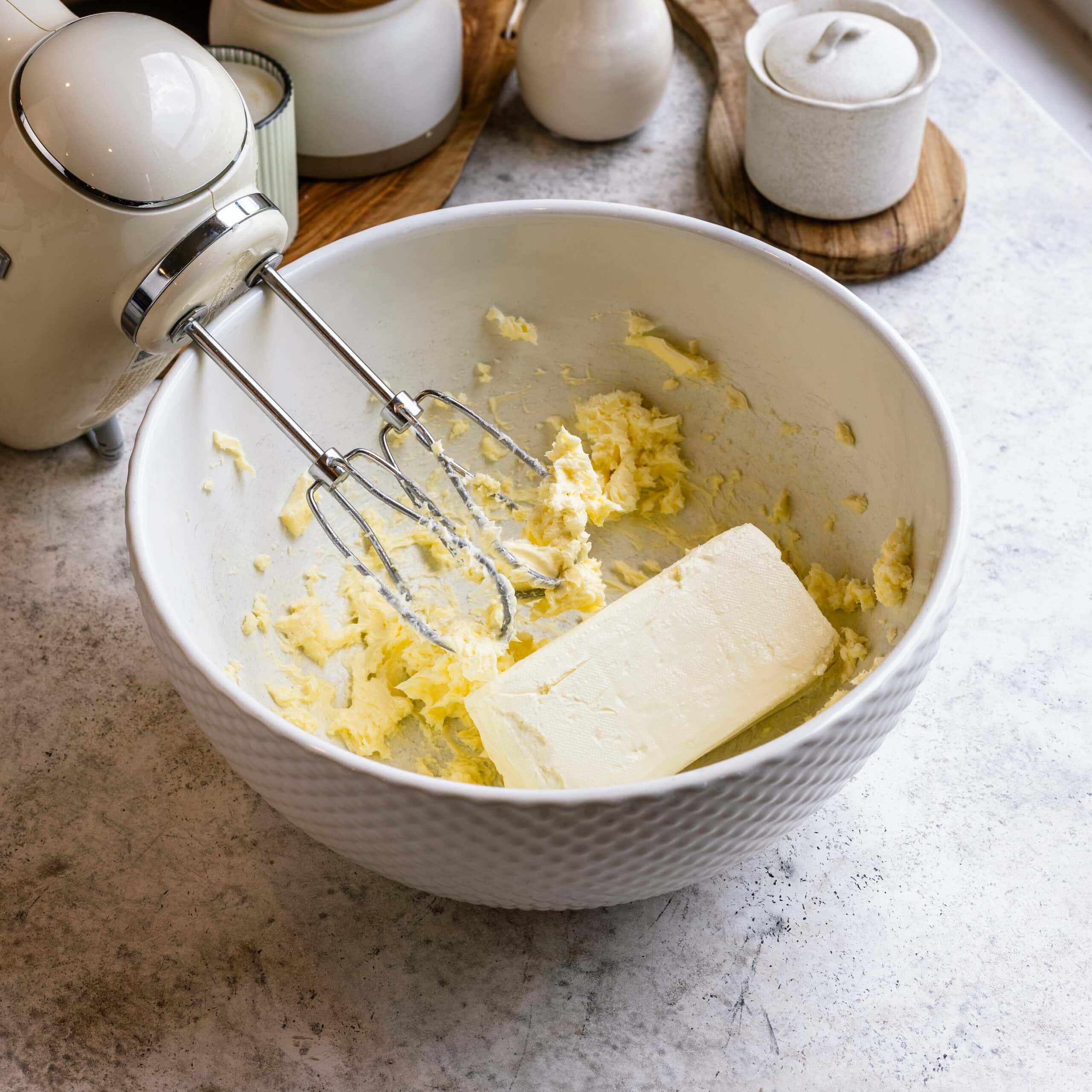 Butter and cream cheese being creamed together in a large mixing bowl.