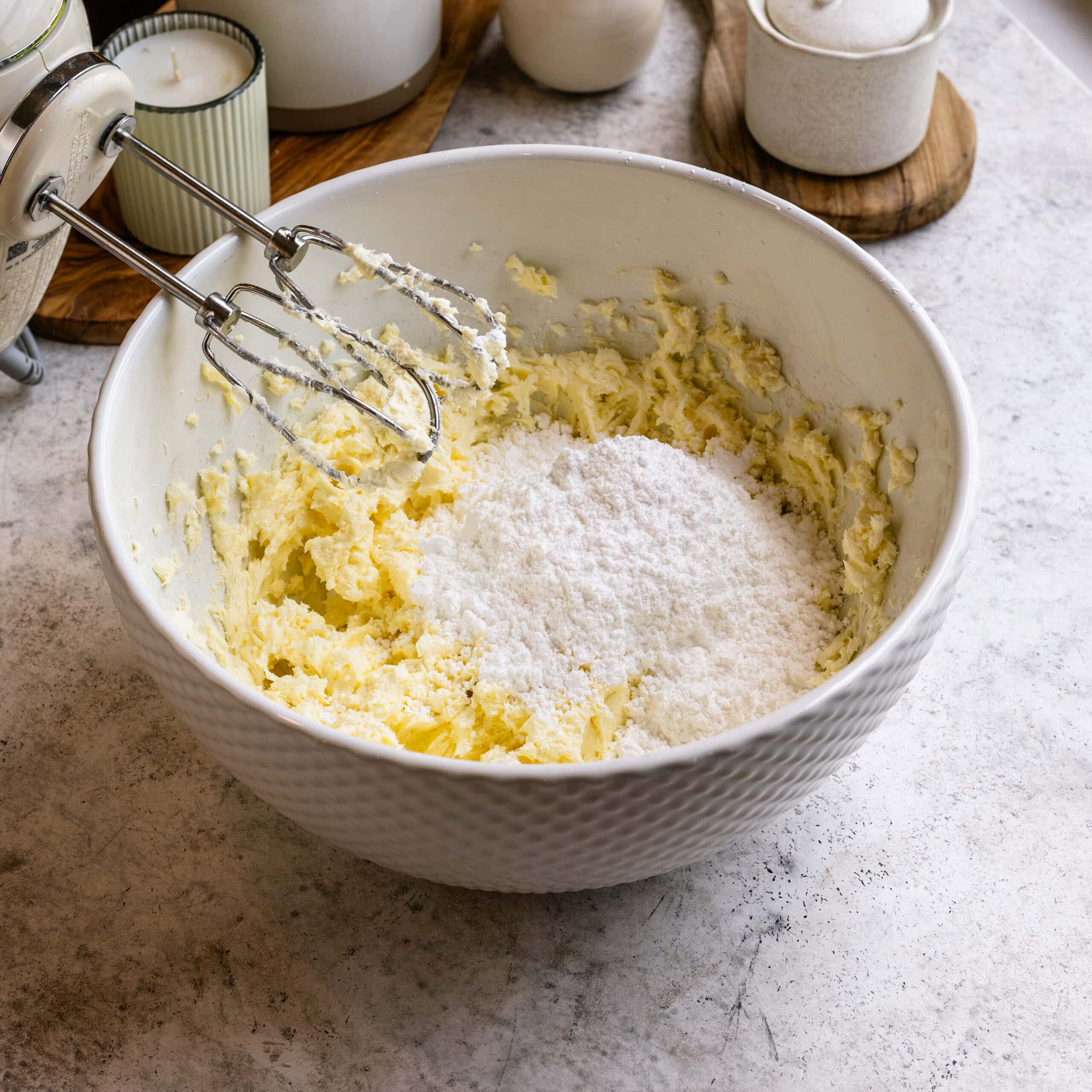 Powdered sugar being added to the creamed butter and cream cheese to make blueberry cream cheese frosting.