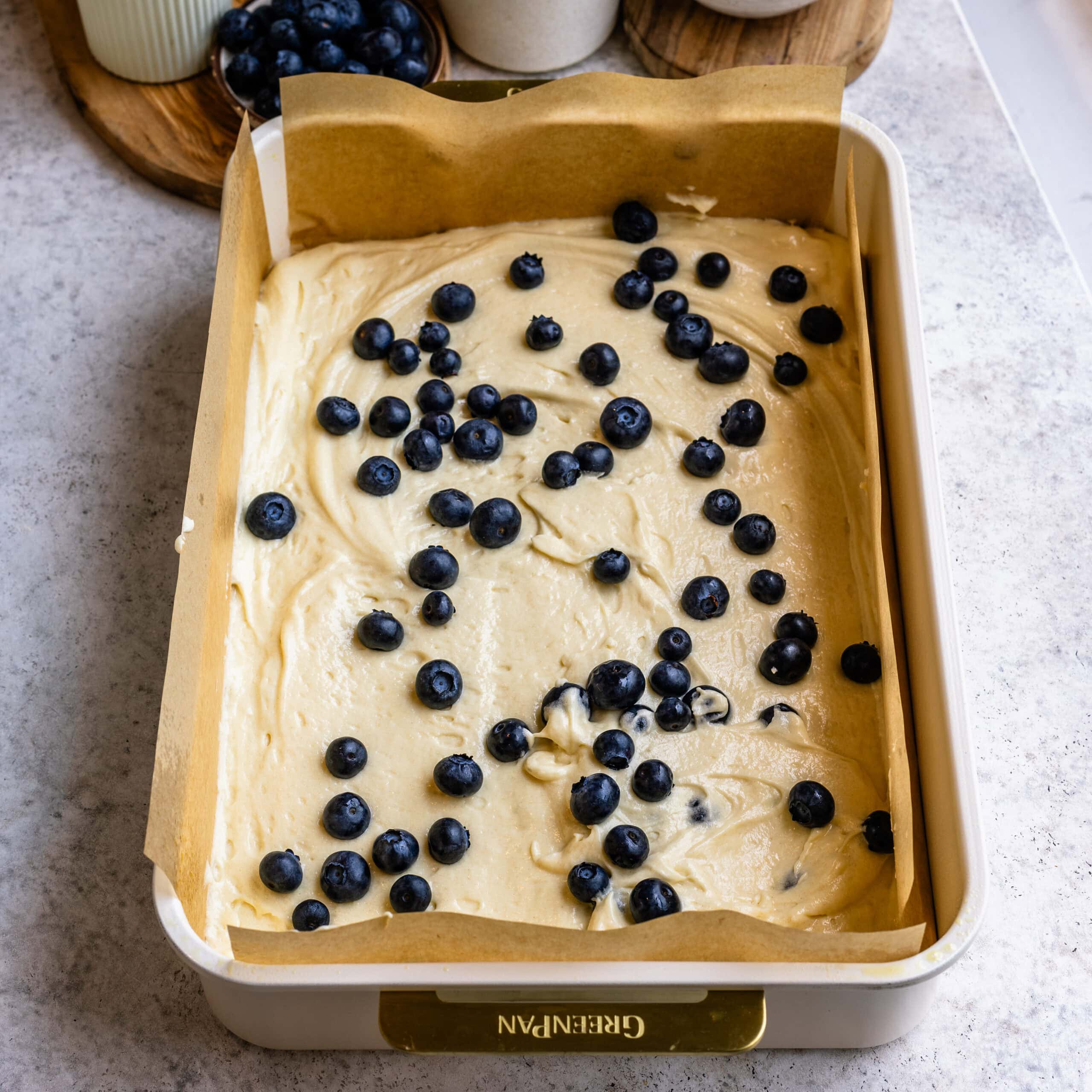 A parchment lined sheet pan with one layer of cake batter, and a sprinkle of fresh blueberries.
