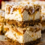 Two stacked Peach Crumble Cheesecake Bars with creamy cheesecake, spiced peach filling, buttery crumble, and cream cheese glaze.