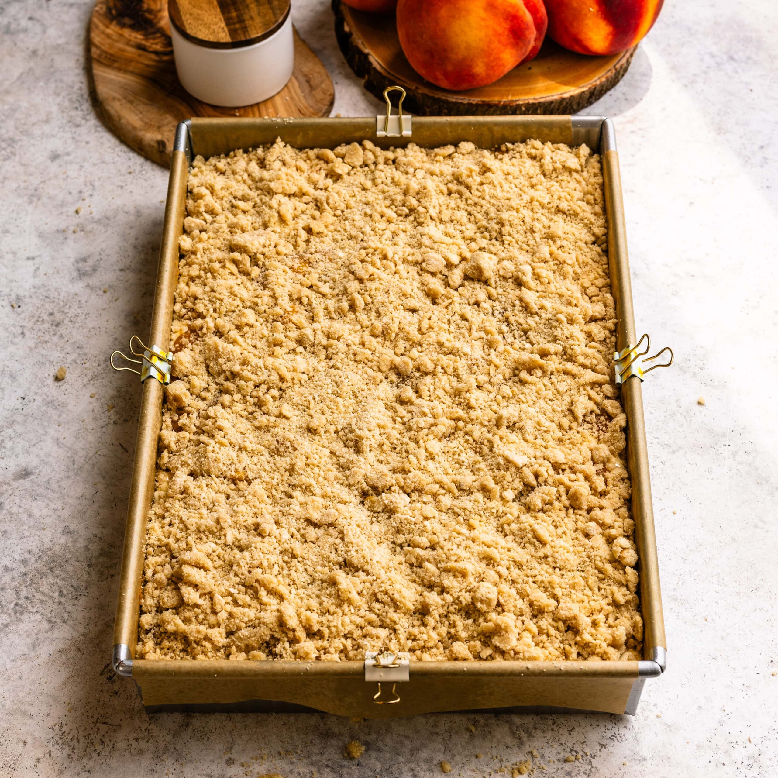 Crumble being added to form the final layer for peach crumble cheesecake bars.