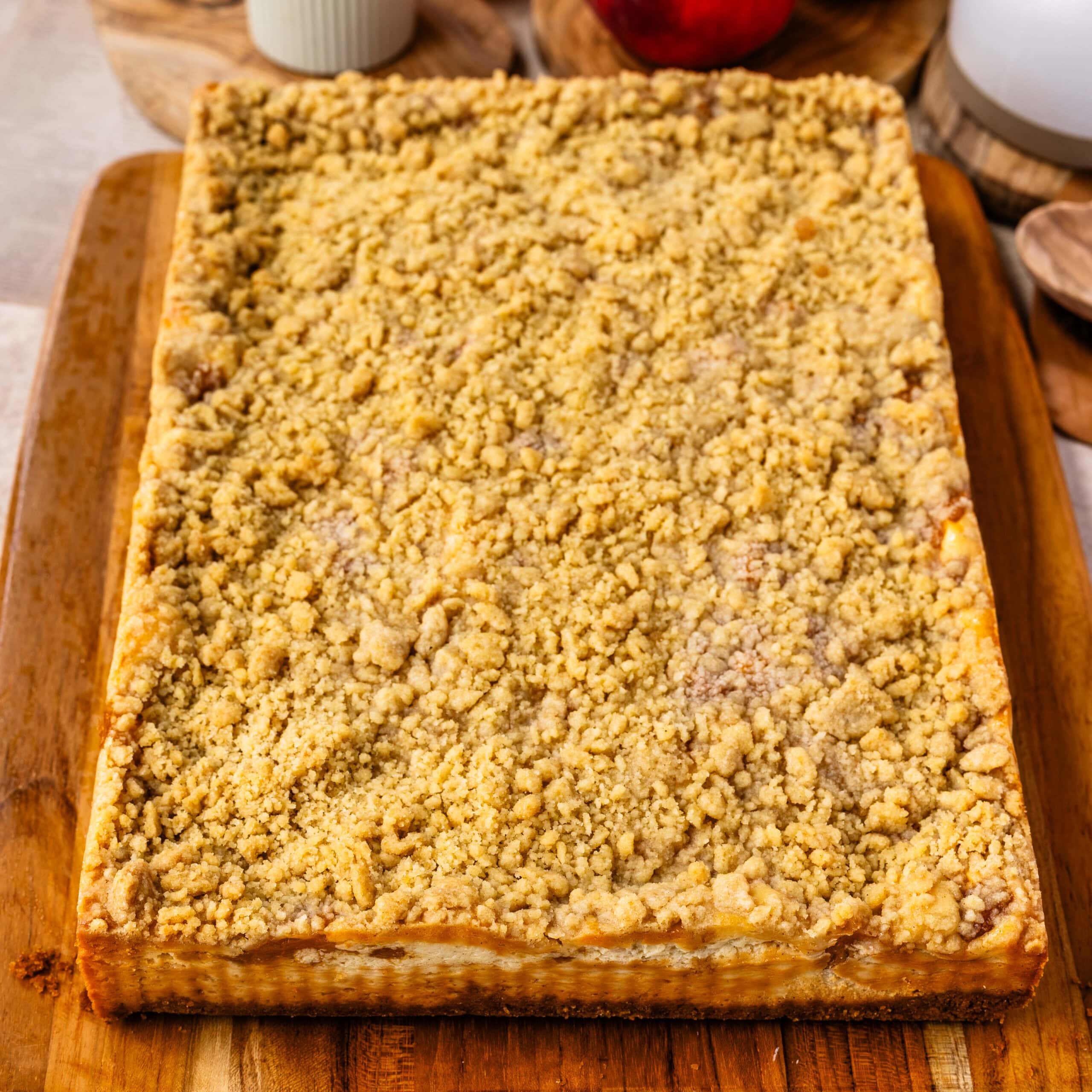 Freshly baked Peach Crumble Cheesecake Bars on a cutting board topped with a golden brown buttery crumble.