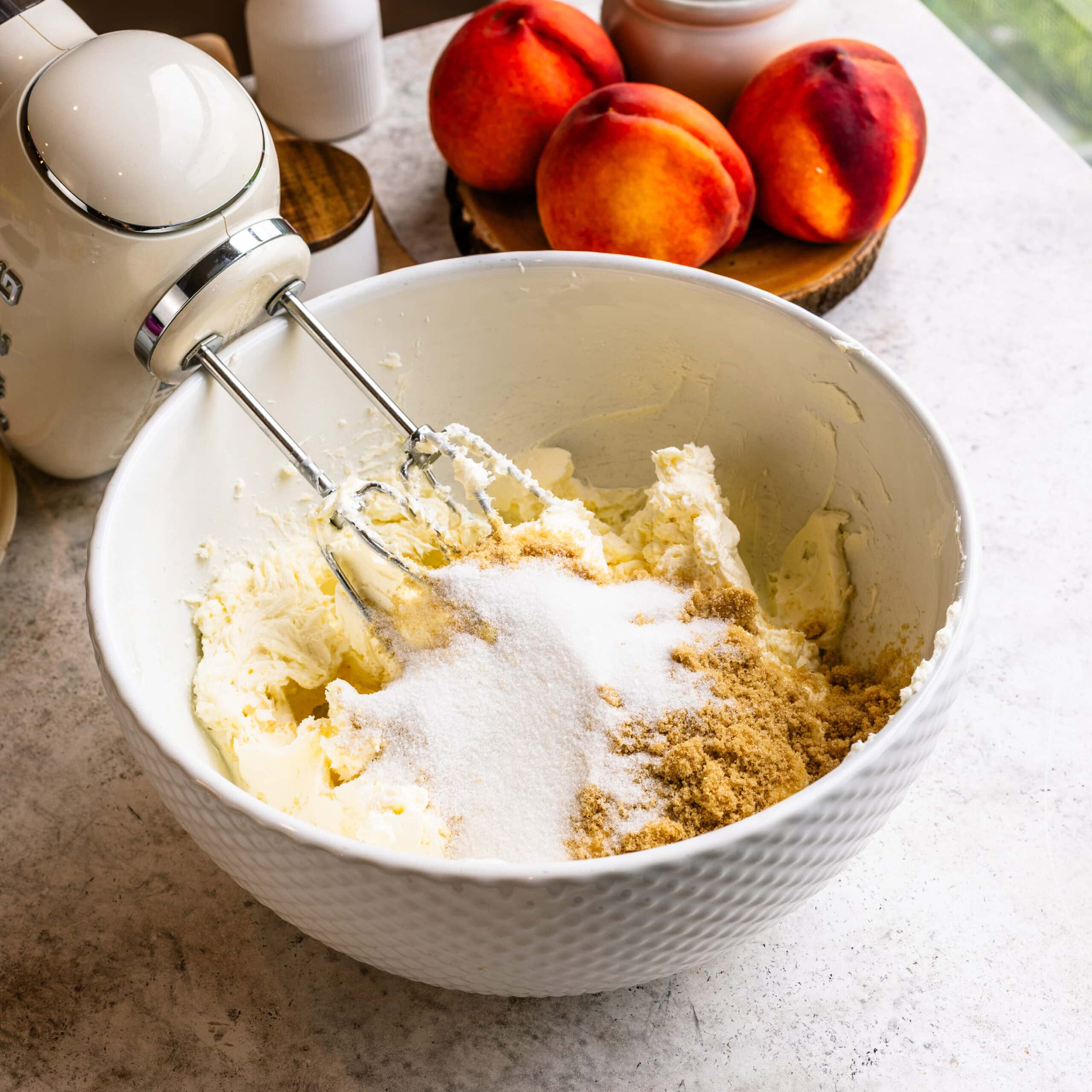 A mixing bowl full of the base ingredients for the peach crumble cheesecake layer. It includes cream cheese, sugar, and brown sugar.