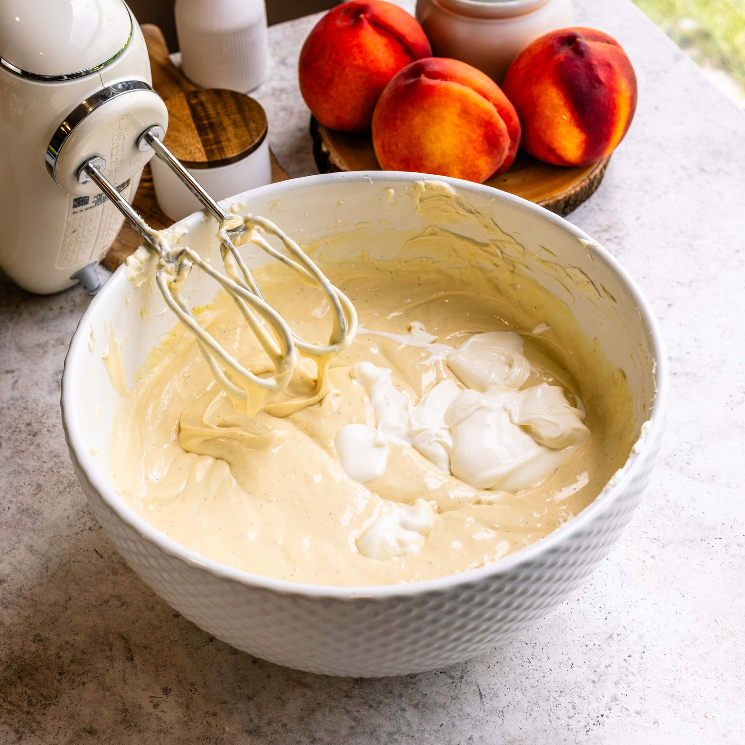 Sour cream being added to the cheesecake batter in a large mixing bowl.