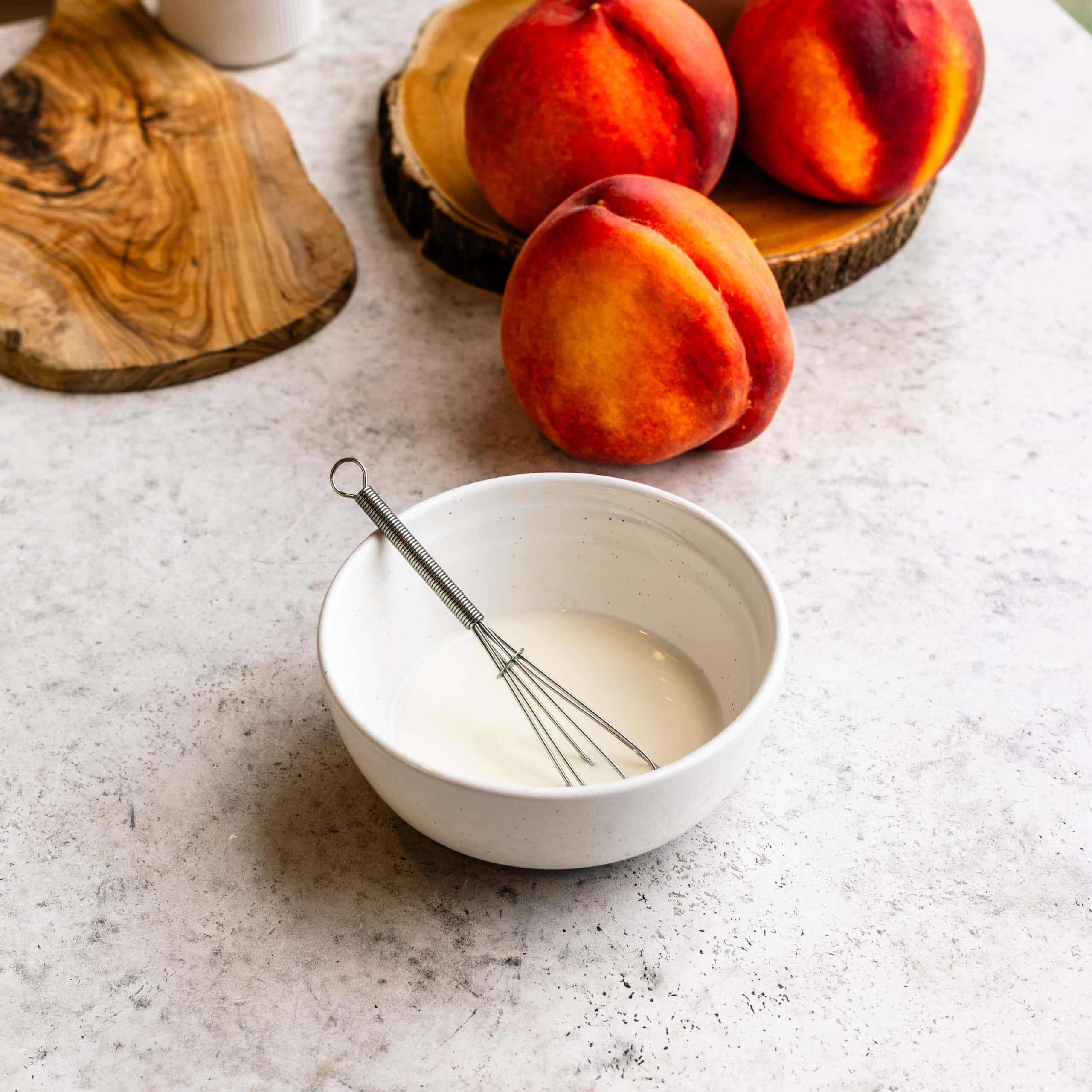 A small bowl of vanilla glaze for peach crumble cheesecake bars.