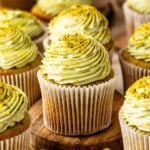 Pistachio cupcakes with pistachio cream cheese frosting and chopped pistachios on a wooden board.