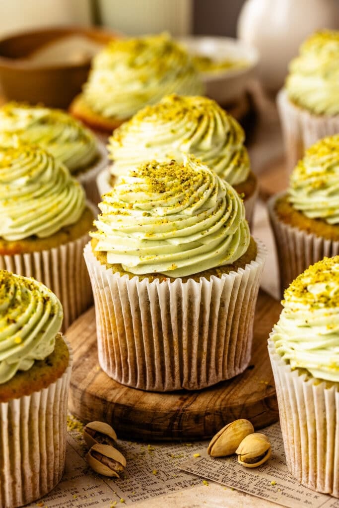Pistachio cupcakes with pistachio cream cheese frosting and chopped pistachios on a wooden board.