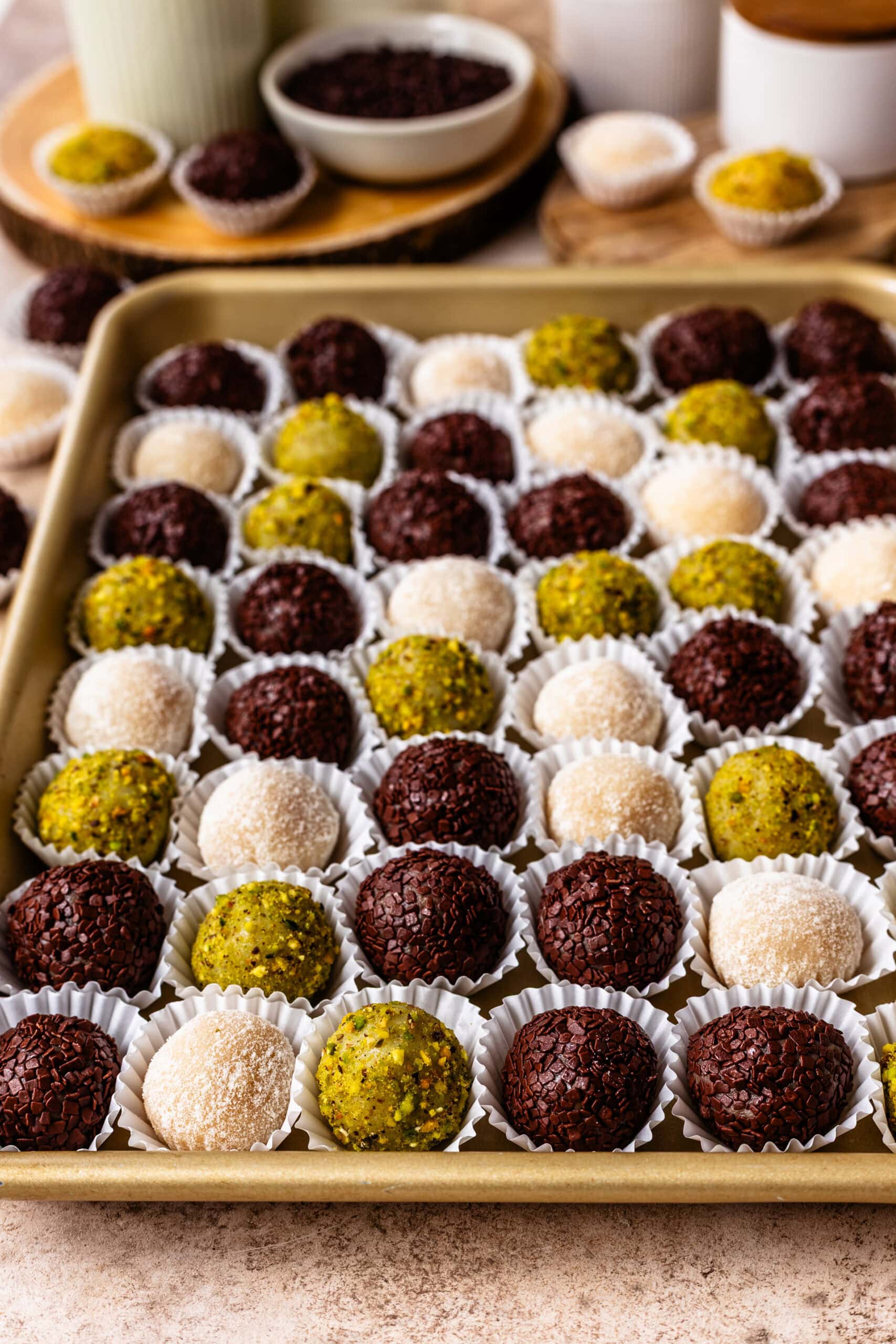 Brazilian chocolate brigadeiros coated in sprinkles, pistachios, and nido powdered milk, and arranged in small paper cups on a baking tray.