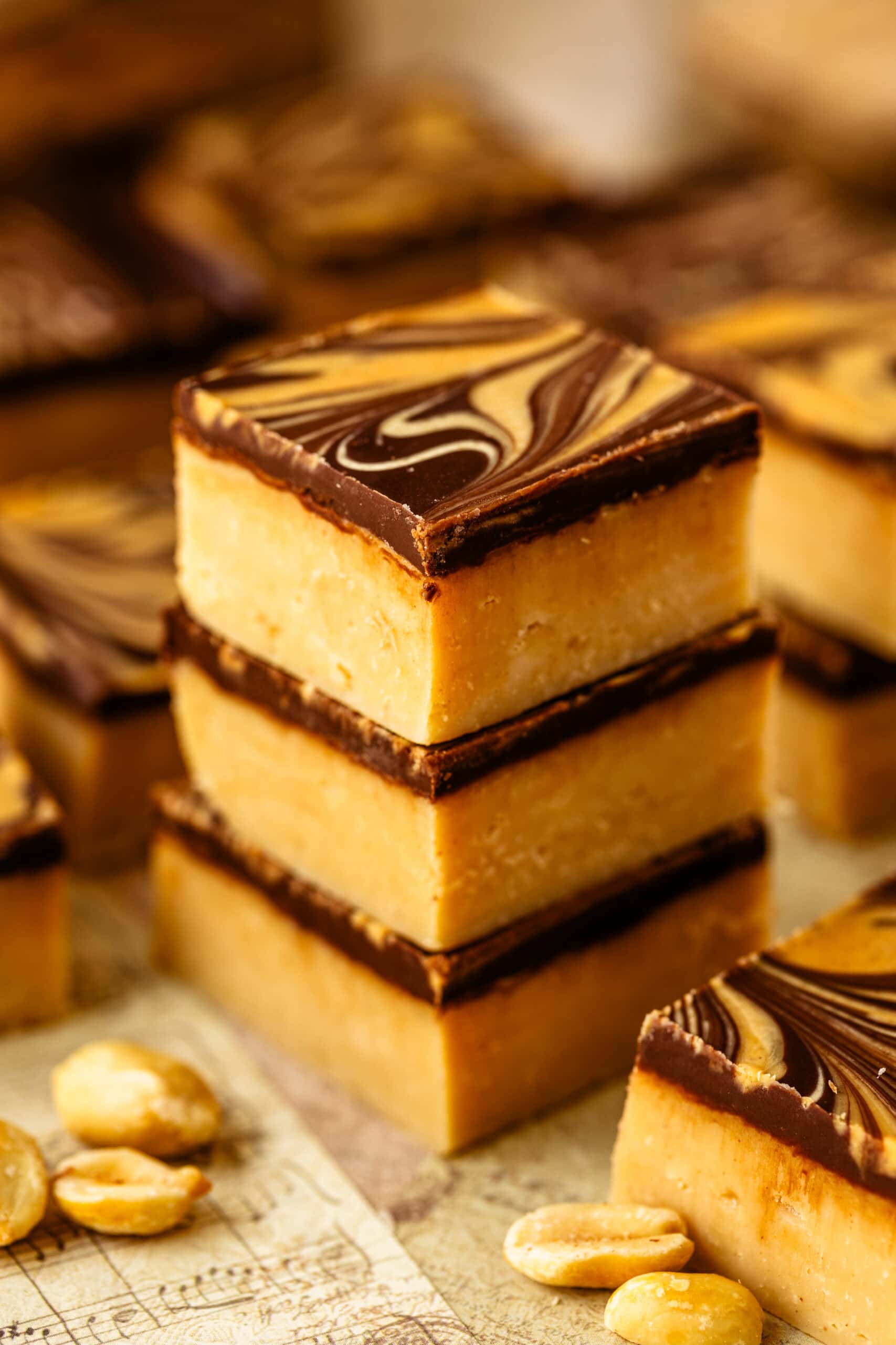 Peanut butter fudge squares with a chocolate layer and peanut butter swirl on top, stacked together.