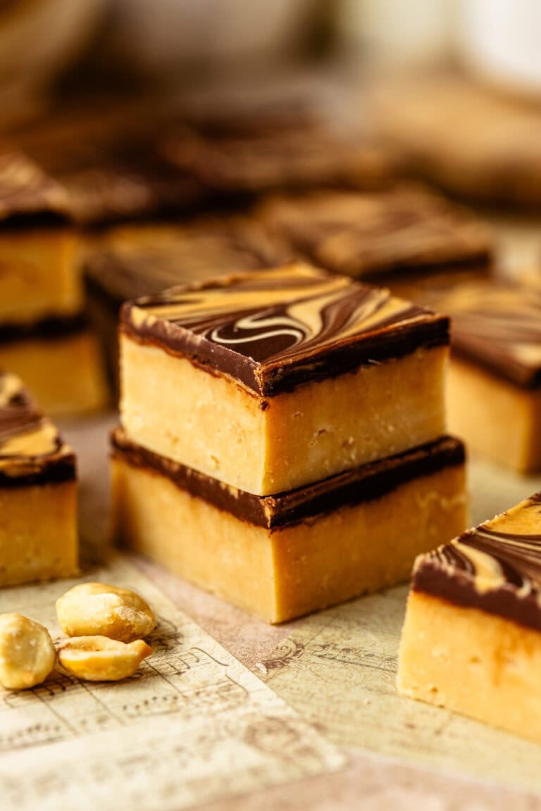 Peanut butter fudge squares with a chocolate layer and peanut butter swirl on top, stacked together.