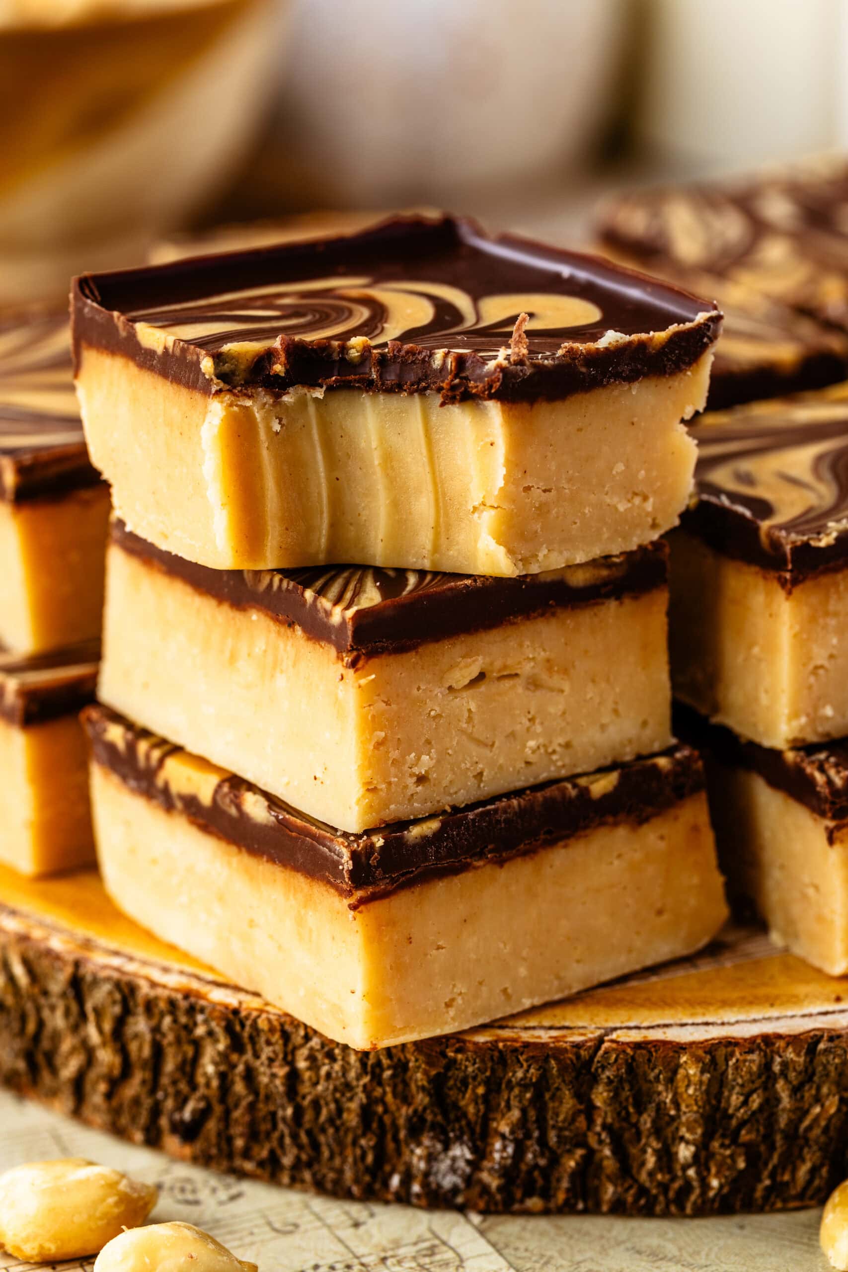 Peanut butter fudge squares with a chocolate layer and peanut butter swirl on top, stacked together.