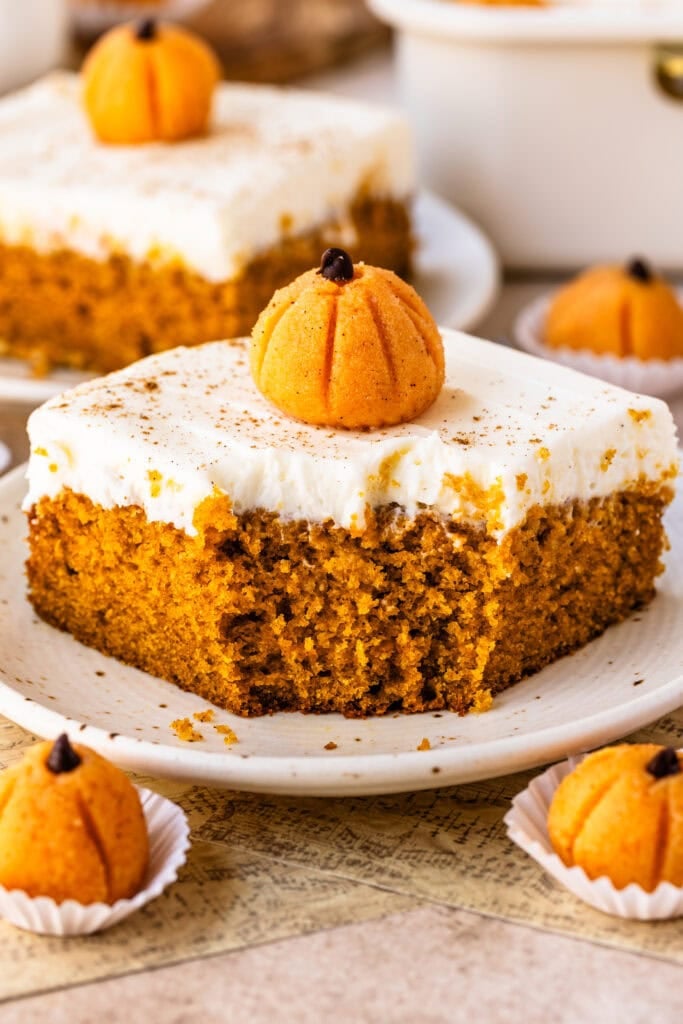 Slice of pumpkin sheet cake topped with cream cheese frosting and a pumpkin brigadeiro.
