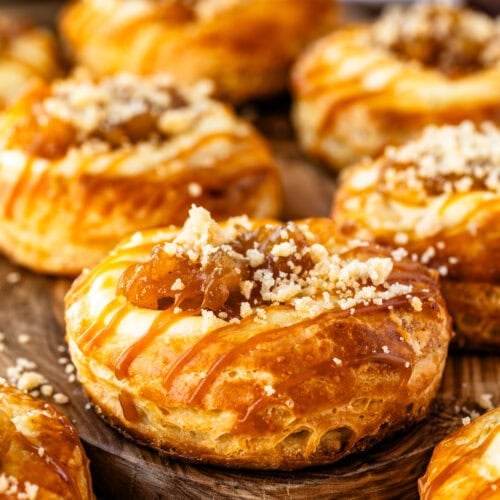 Close-up of a homemade apple Danish topped with cream cheese, cinnamon apple filling, streusel crumbs, and caramel drizzle.